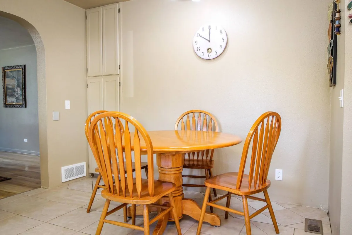 A cozy dining nook with a wooden dining table and four chairs, softened by warm light and a vintage wall clock. The setup encourages shared meals, conversations, and casual gatherings, echoing the section’s emphasis on comfort and family connection.