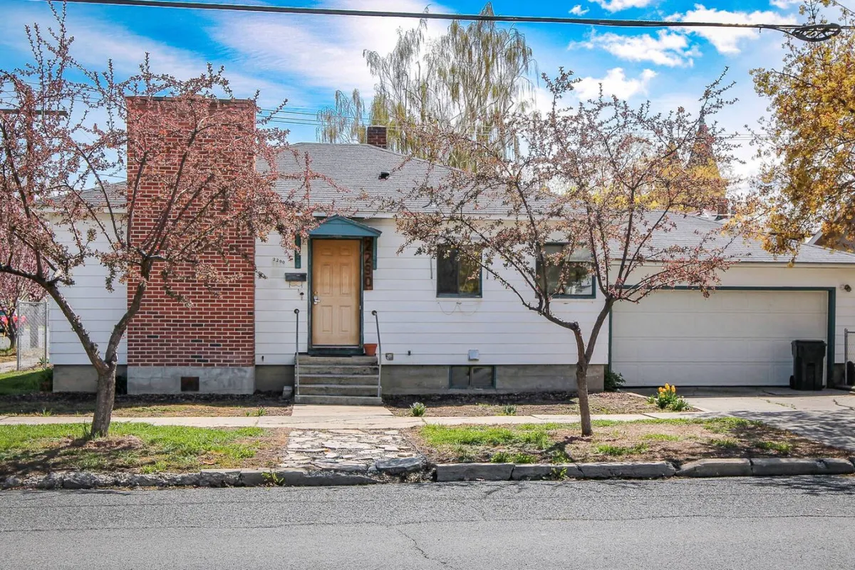 The photo showcases a welcoming residential exterior with a charming front door framed by blooming cherry blossom trees and a classic brick chimney. The inviting yard hints at a peaceful and walkable neighborhood, echoing the historic and picturesque atmosphere described in the section.