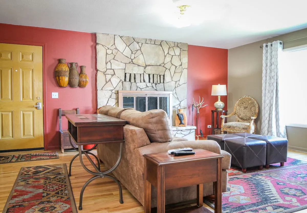 This inviting living room features a striking stone fireplace, a cheerful yellow front door, and stylish decor including decorative vases and a cozy armchair. The scene radiates warmth and charm, suggesting a space perfect for relaxing, gathering with loved ones, and making lasting memories.